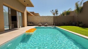 Una piscina con un muro de piedra y una zona ajardinada.