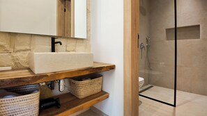 Un baño con pared de piedra, tocador de madera, lavabo blanco y cabina de ducha de vidrio.