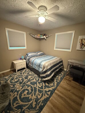 Una camera da letto con un letto, un comodino, una scrivania e una ventola a soffitto.
