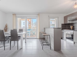Une cuisine moderne avec un coin repas, un balcon avec des chaises bleues et une vue sur les immebles.
