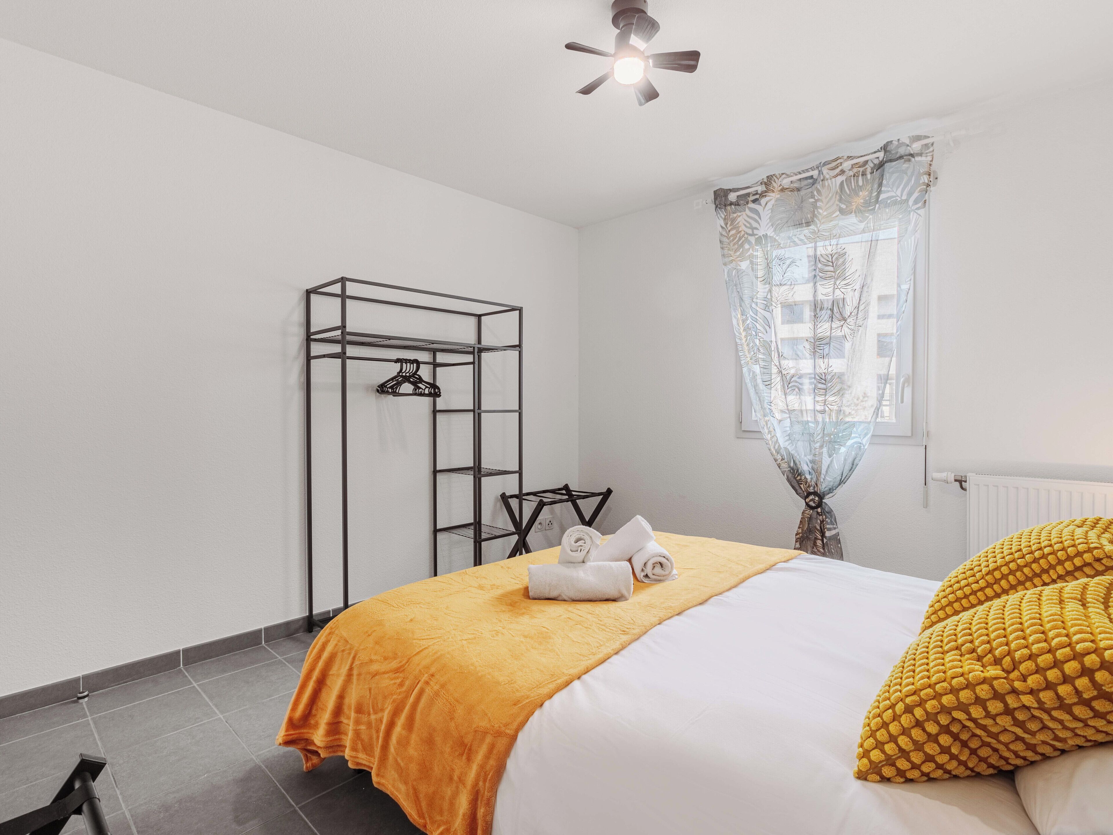 A hotel room with a bed, a wardrobe, a ceiling fan, and a window with sheer curtains.