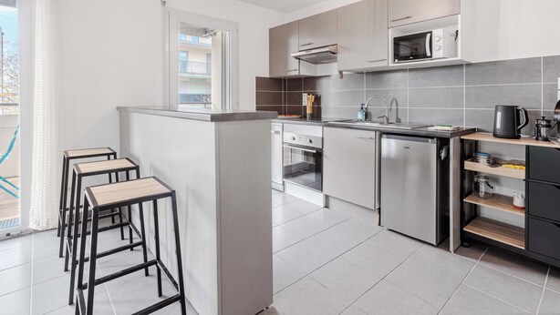 A modern kitchen with a central island, built-in appliances, and a view to the outside. - Appartement calme et lumineux, terrasse et P privé (Balma)