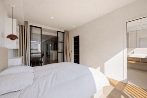 A modern bedroom with a large bed, a desk, and a bathroom with a mirror and sink. - Cocoon with Eiffel Tower view (Paris)