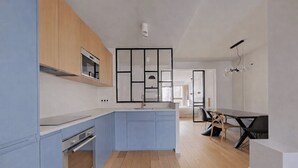 A modern kitchen with blue cabinetry, a central island, and a dining area with a table and chairs. - Cocoon with Eiffel Tower view (Paris)