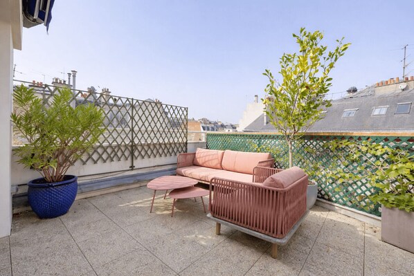 A rooftop terrace with a sofa, two chairs, a potted plant, and a decorative fence. - Cocoon with Eiffel Tower view (Paris)