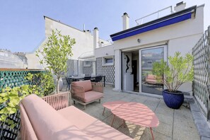 Une terrasse sur le toit, aménagée avec du mobilier d’extérieur, un pot de fleurs et une porte-fenêtre coulissante donnant sur un espace intérieur.