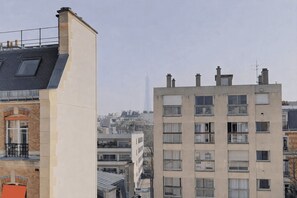A multi-story building with balconies, a brick facade, and a clear view of the city skyline in the background. - Cocoon with Eiffel Tower view (Paris)