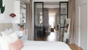 A modern hotel room with a large bed, a desk, and a glass door leading to a dining area. - Cocoon with Eiffel Tower view (Paris)