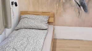 Un dormitori amb un llit, un panell de fusta al capçal, un mural del mur amb un ocell i un paviment de fusta.