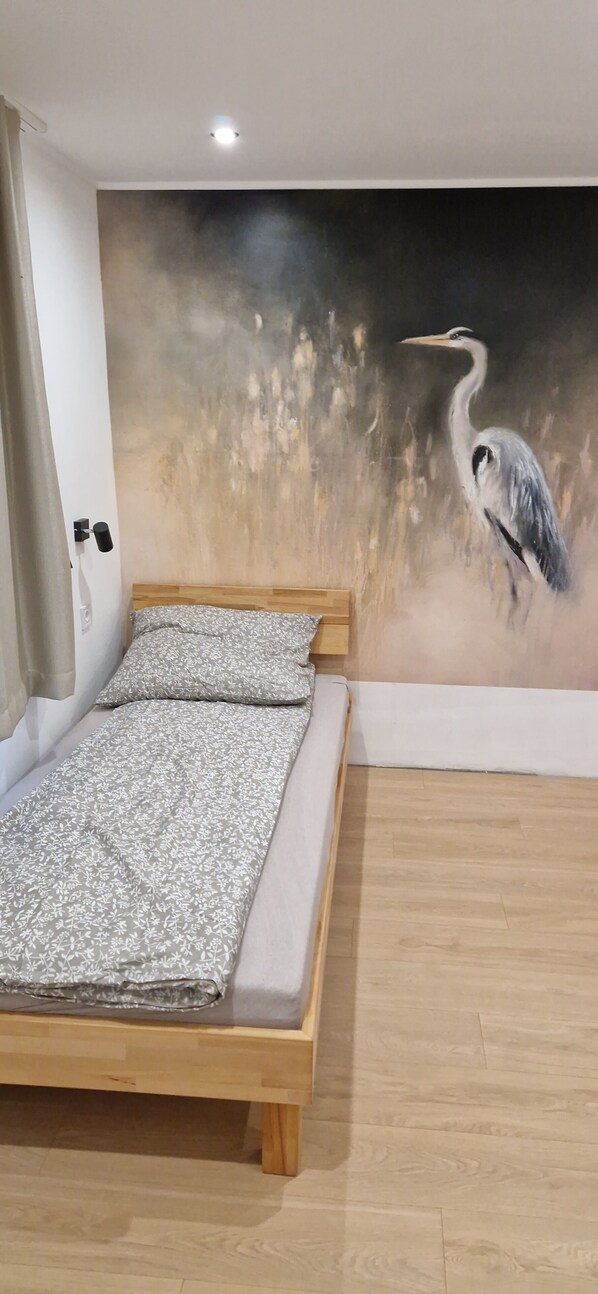 A bedroom with a bed, a wooden headboard, a wall mural of a bird, and a wooden floor.