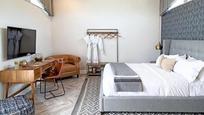 A modern hotel room with a bed, a desk, a chair, a TV, and a coat rack with clothes. - New Pulka beautiful apartment in Riga (Riga)