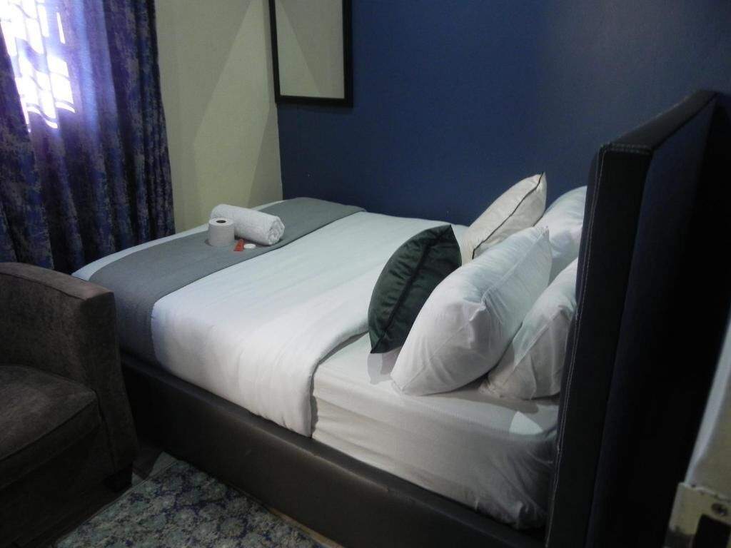 A hotel room with a bed, a chair, a window with curtains, and a mirror on the wall.