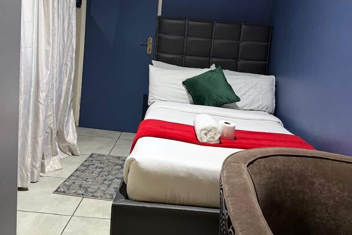 A bedroom with a bed, a chair, a door, and a curtain.
