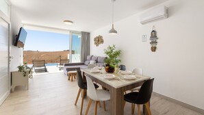 A dining area with a wooden table, white and black chairs, a plant centerpiece, and a view of a desert landscape through large windows. - Villa Papaya by Escape Home (Tías)