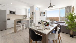A modern kitchen with white cabinets, a dining area with a table set for four, and a large window offering a view of the landscape. - Villa Papaya by Escape Home (Tías)