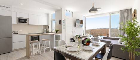 A modern kitchen with white cabinets, a dining area with a table set for four, and a large window offering a view of the landscape.