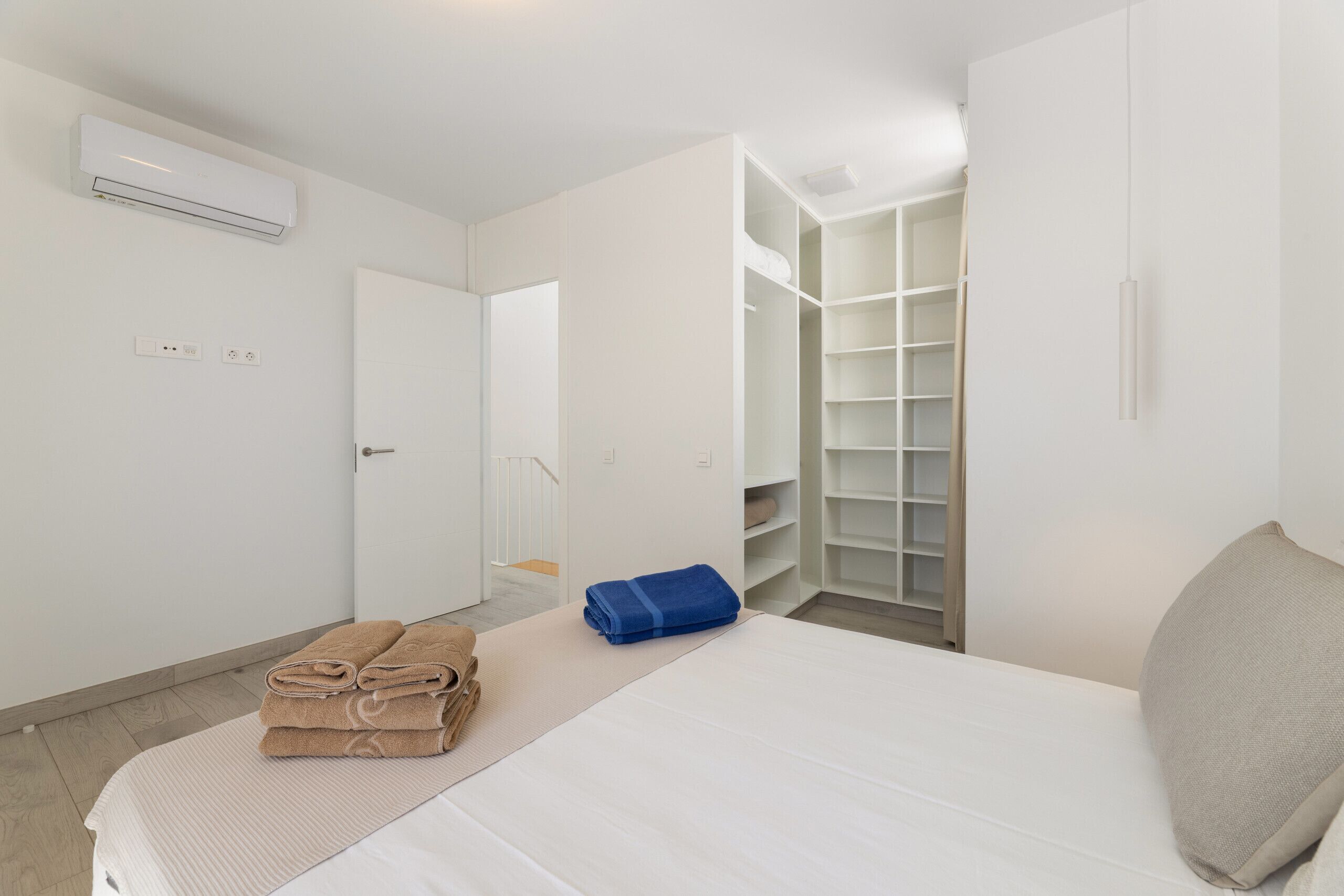 A hotel room with a bed, a wardrobe, a closet, and an air conditioning unit.