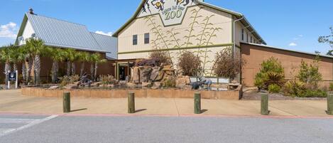 A building with a sign reading "Baja Maya Gulf Coast Zoo" and a parking lot in front.