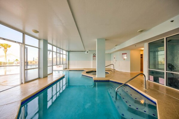 An indoor swimming pool with clear glass walls, a tiled floor, and a pool ladder. - The Dunes 100 (Gulf Shores)