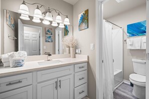 A bathroom with a white sink, a mirror, and a shower curtain. - The Dunes 100 (Gulf Shores)