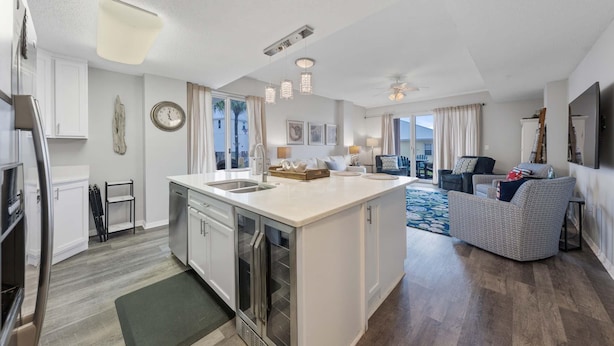 A modern kitchen with a central island, a dining area with a sofa, and a living room with a TV. - The Dunes 100 (Gulf Shores)