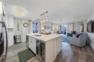 Una cocina moderna con una isla central, un comedor con sofá y una sala de estar con televisor.