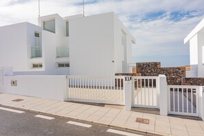 A modern white building with a gated entrance, a stone wall, and a clear sky. - Villa Mandarina by Escape Home (Tías)