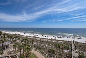 A beach with a wooden boardwalk, palm trees, and beach umbrellas. - Indigo West 502 (Pensacola)