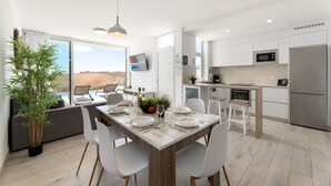 Een moderne keuken met witte kasten, een roestvrijstalen koelkast en een eethoek met een houten tafel en witte stoelen.