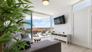 Een moderne woonkamer met een bank, een televisie, een schuifdeur naar een buitenruimte en een kleine tafel.