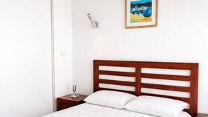 A bedroom with a large bed, wooden headboard, two bedside tables, a nightstand, a wall-mounted light, and a framed picture. - LVAM - Appartement Résidence St Clair - Piscine - 4 personnes - Cap d'Agde (Le Cap D'Agde)
