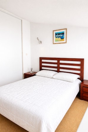 Un dormitorio con una cama grande, cabecera de madera, dos mesitas de noche, un velador y una lámpara de pared, además de un cuadro enmarcado.