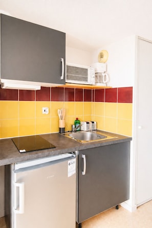 Una cocina compacta equipada con microondas, cafetera y refrigerador pequeño.