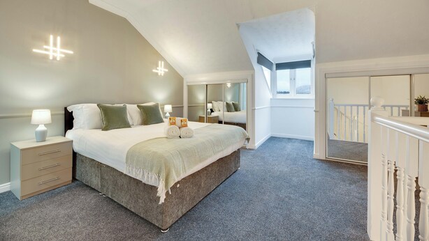 Quarto com cama grande, mesas de cabeceira, espelho e vista para o exterior.
