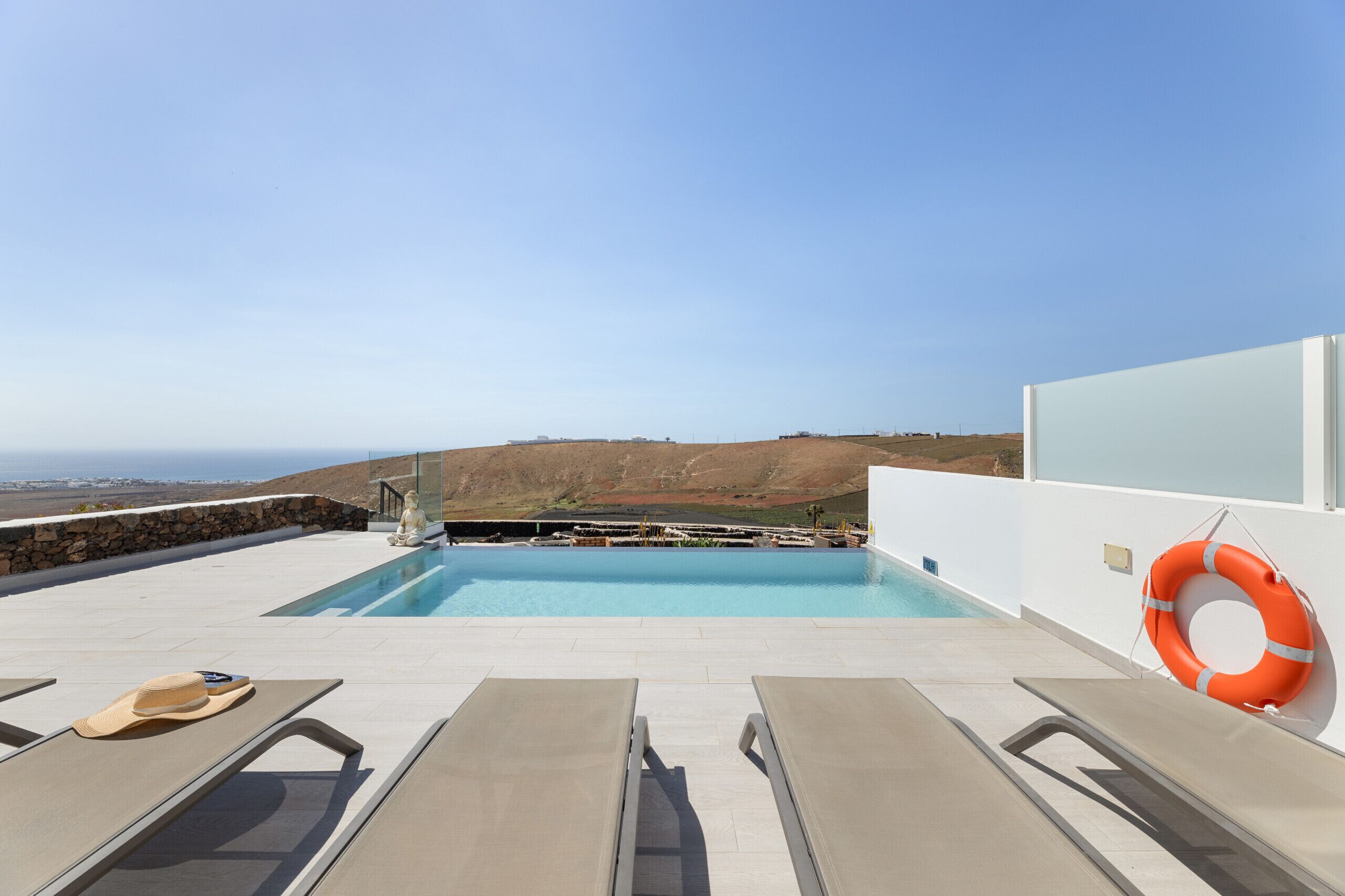 A pool with a view of the landscape, lounge chairs, and a lifebuoy.