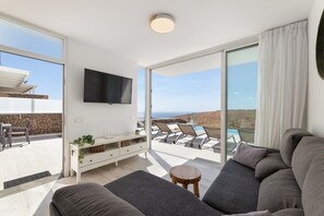 A modern living room with a sofa, a small table, a TV mounted on the wall, and a balcony with a pool and chairs. - Villa Maracuya by Escape Home (Tías)