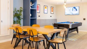 Ein Zimmer mit Poolbillard, einem Esstisch mit Stühlen, einem Bücherregal und gerahmten Bildern an der Wand.