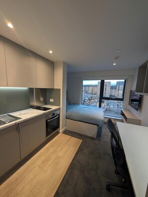 A modern apartment with a kitchen, a bed, and a view of the city. - Student Only West End (Glasgow)