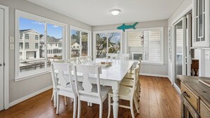 A dining room with a large table and white chairs, large windows, and a view of neighboring houses. - Waterfront 5 bedroom vacation retreat in South Bethany (South Bethany)