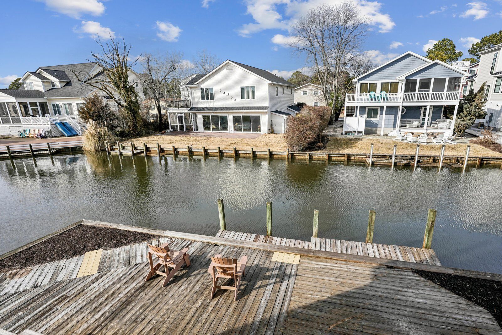 A waterfront property with a dock, wooden chairs, and houses with balconies.