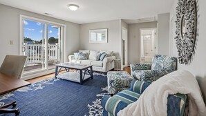 A living room with a sofa, armchair, coffee table, and a view through a sliding door to the outside. - Waterfront 5 bedroom vacation retreat in South Bethany (South Bethany)