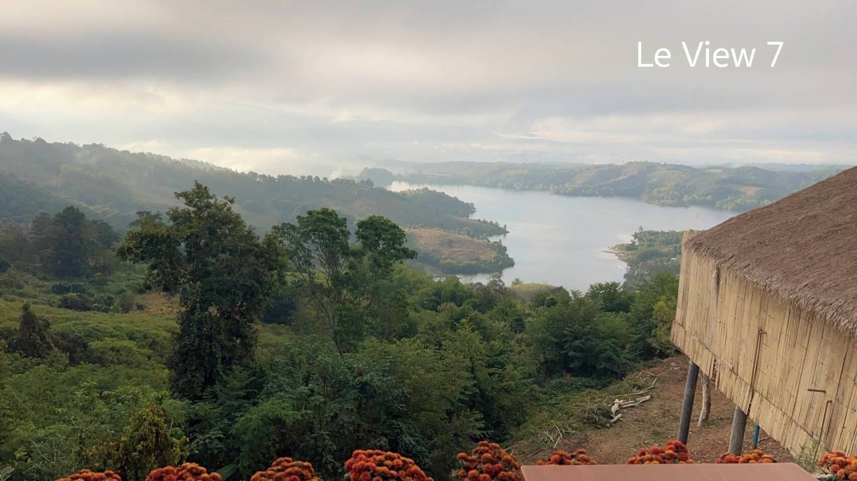 A scenic view of a lake surrounded by lush greenery and a traditional thatched-roof structure.