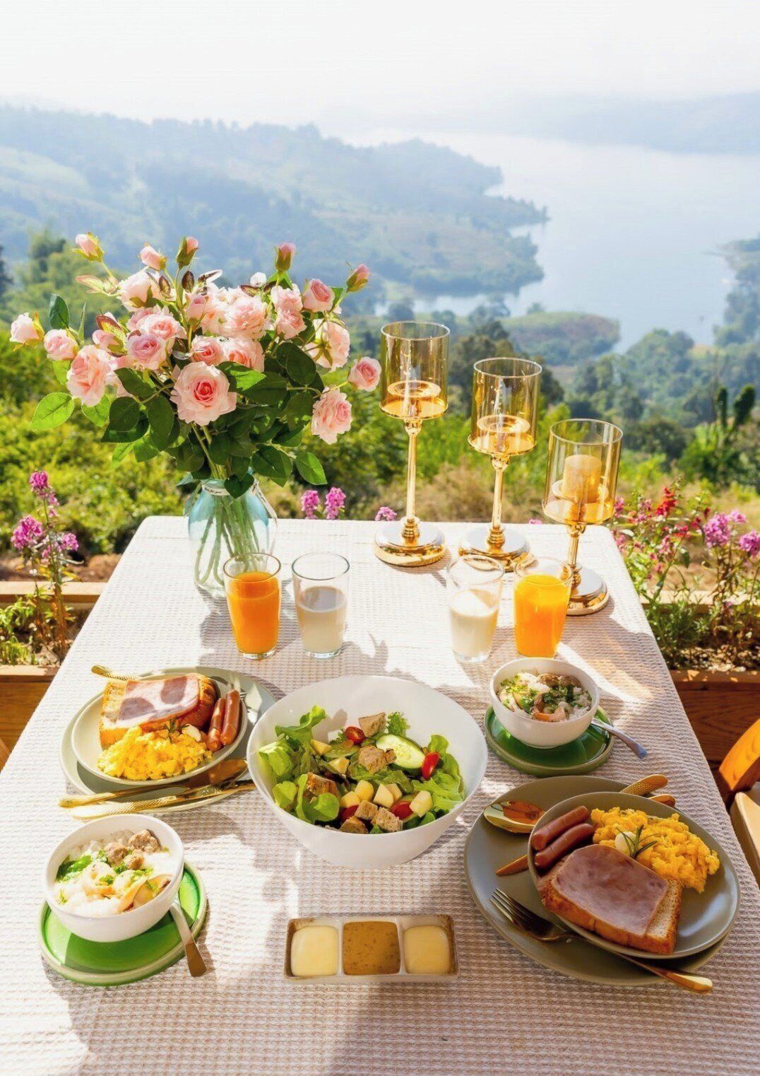 A table set for breakfast with various dishes, a vase of flowers, and glasses of orange juice.