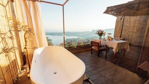 Ein Badezimmer mit einer freistehenden Badewanne, einem Holztisch mit Stühlen und Seeblick.