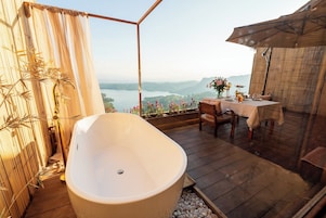 Une salle de bain avec une baignoire sur pieds, une table en bois avec des chaises et une vue sur un lac.