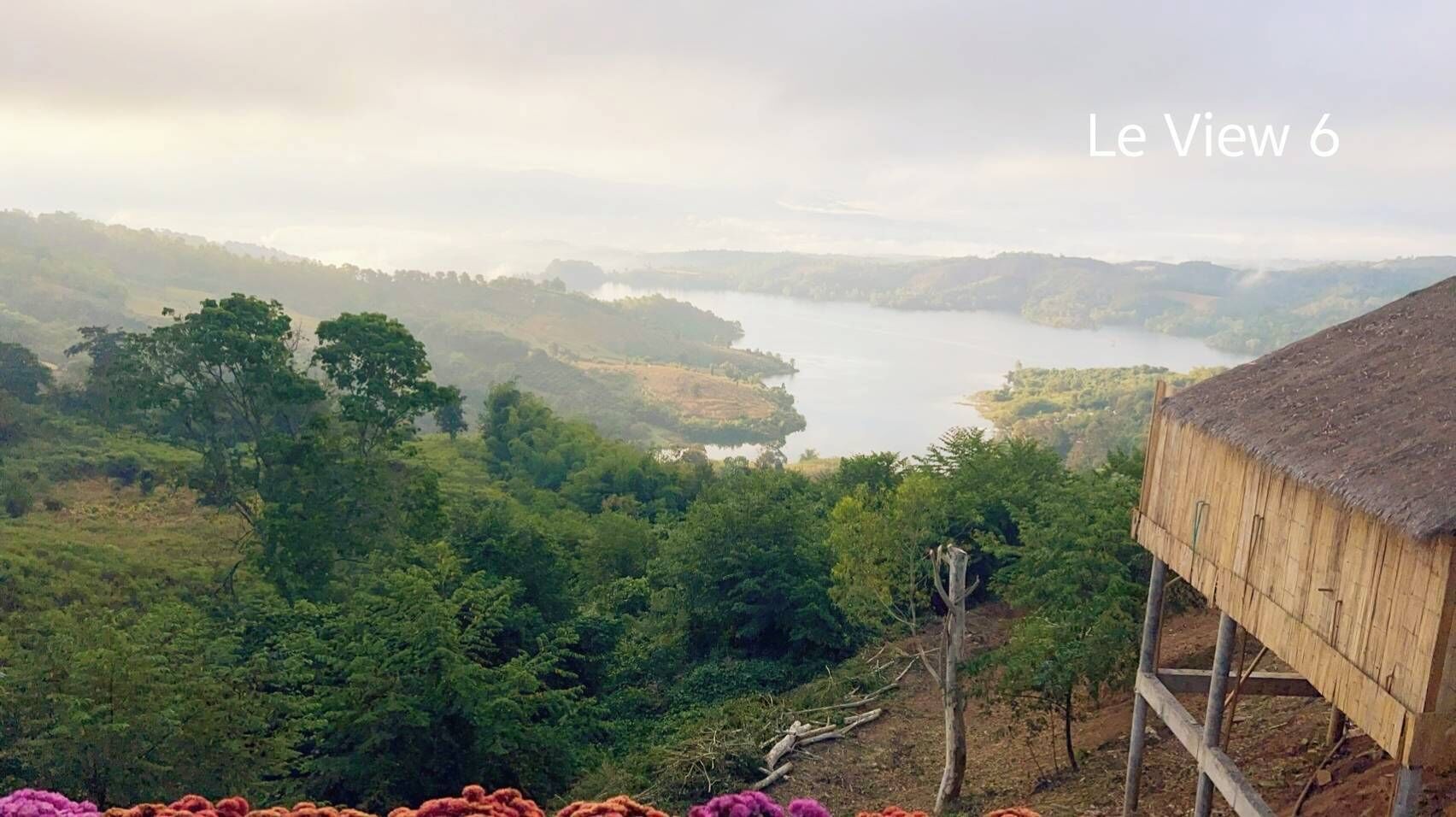 A rustic wooden structure with a thatched roof overlooking a lush valley and a lake.
