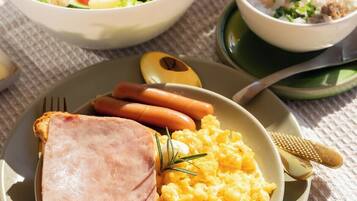 A breakfast plate with ham, scrambled eggs, and toast, a bowl of salad, and a glass of orange juice.