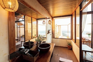 Une pièce de style japonais traditionnel, avec un sol recouvert de tatamis, une basse table en bois sur laquelle sont posés des bols, et une vue sur la mer par de grandes fenêtres.