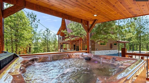 Un espace avec un bain à remous, doté d’une terrasse en bois, entouré d’une structure de cabane en bois et d’arbres.