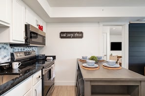 A modern kitchen with a microwave, oven, and a dining table set with bowls and plates. - The Landing Loft! Walk to Downtown, Pools, Fishing, Gym, Scenic Train Station.. (Branson)